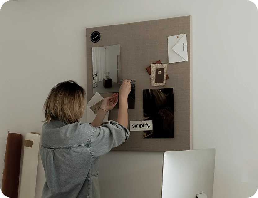 Frau von hinten, welche verschediene Bilder an eine Pinnwand hängt