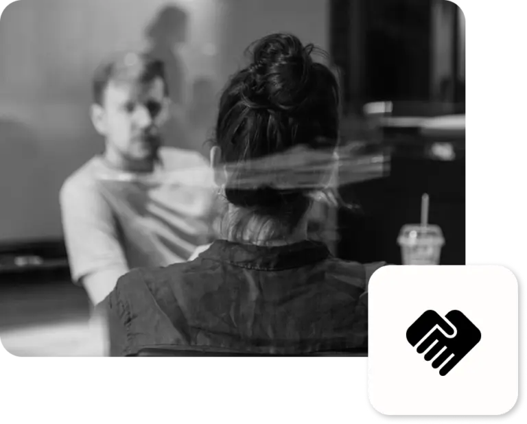 Ein Mann und eine Frau hinter einer Scheibe, die sitzend zu einem Corporate Design diskutieren