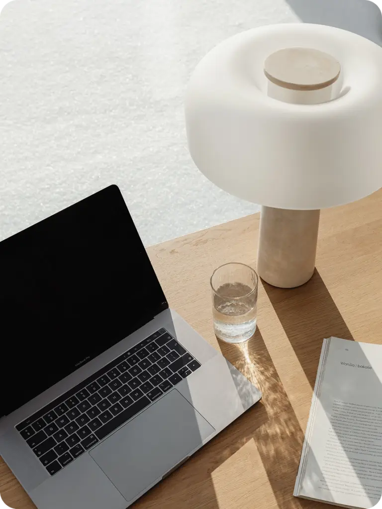 Sonniger Arbeitsplatz einer Brand Designerin, bestehend aus Laptop einem Glas Wasser und einer Tischleuchte